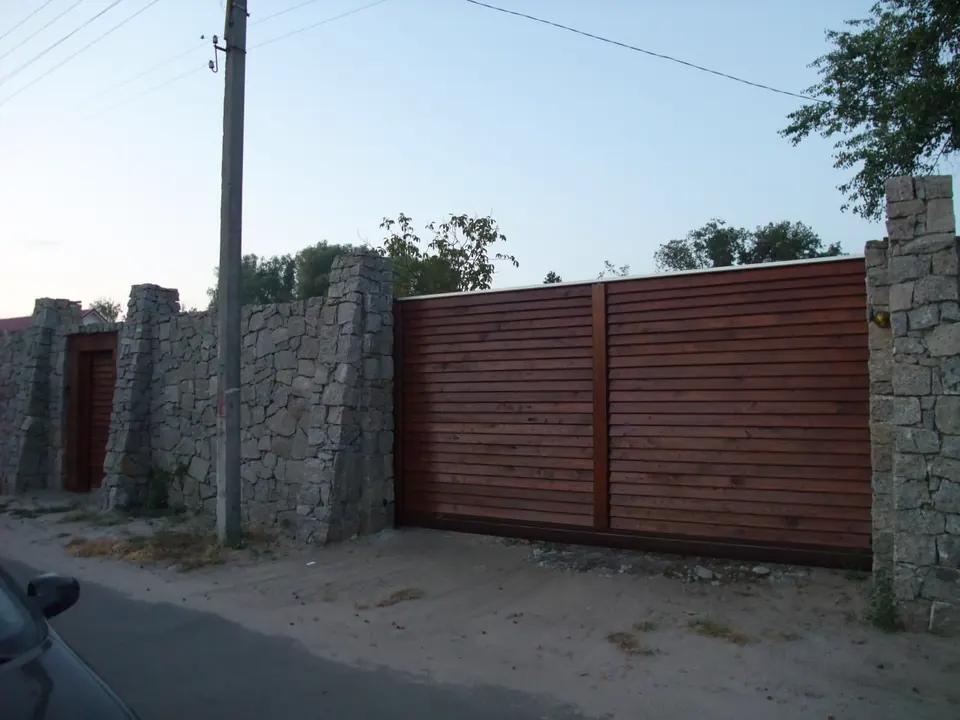 Posuvná brána z vodorovných dřevěných prken v kamenné zdi, pohled z ulice