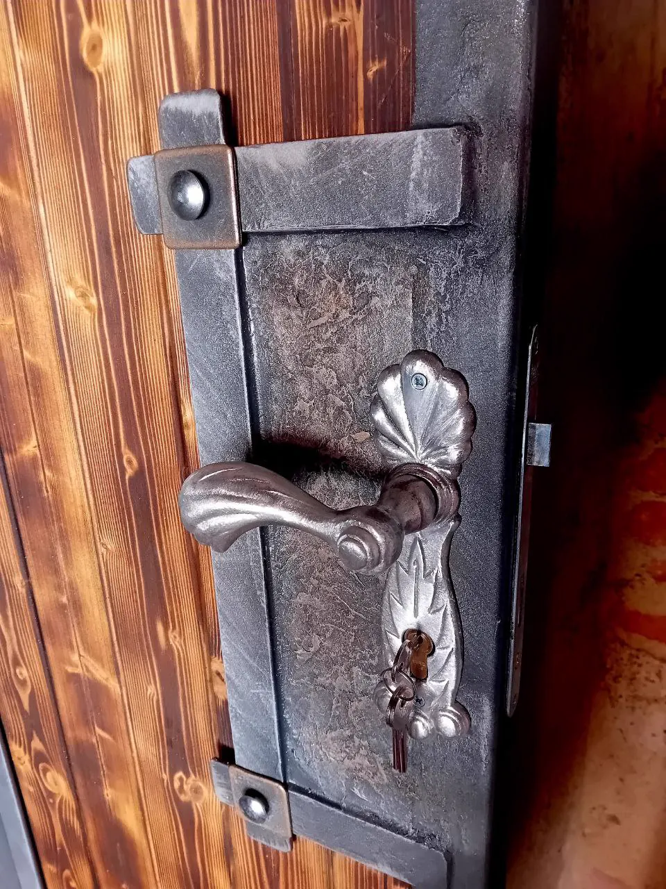 Detail ručně kovaného kování na opáleném dřevu