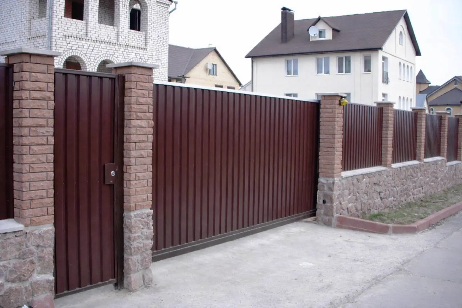 Hnědá posuvná brána a branka z trapézového plechu se sloupky ze štípaných tvarovek a navazujícím plotem
