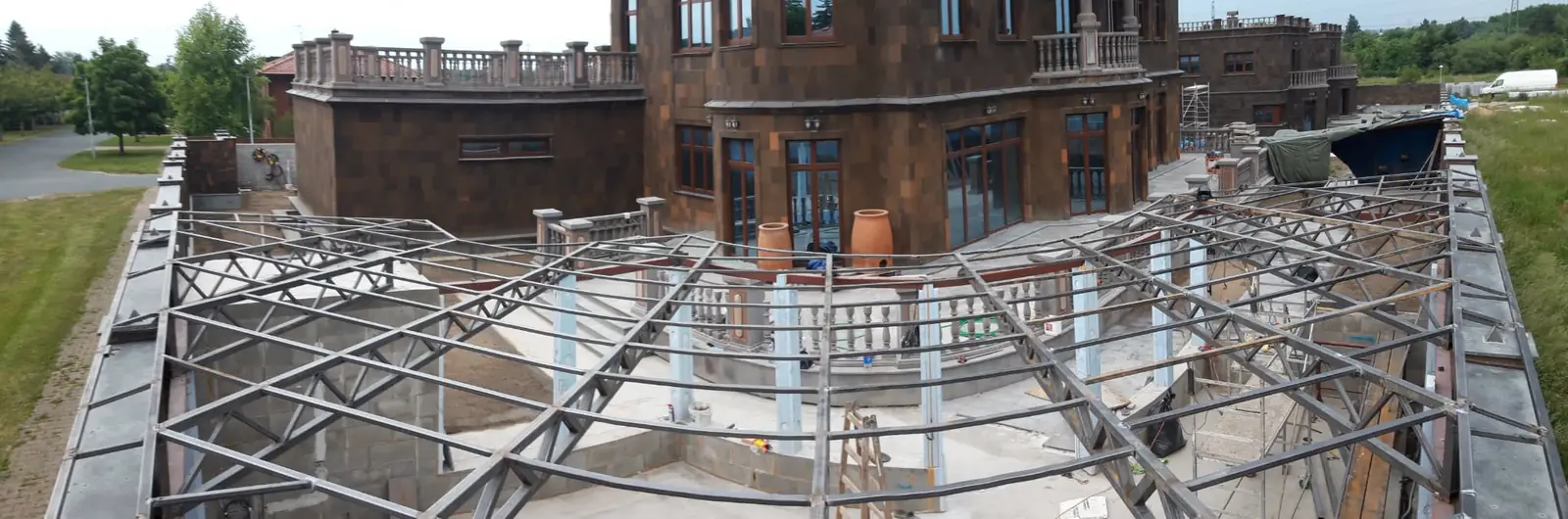 Ocelová příhradová konstrukce zastřešení terasy u velké vily s kamenným obkladem během montáže, panoramatický pohled