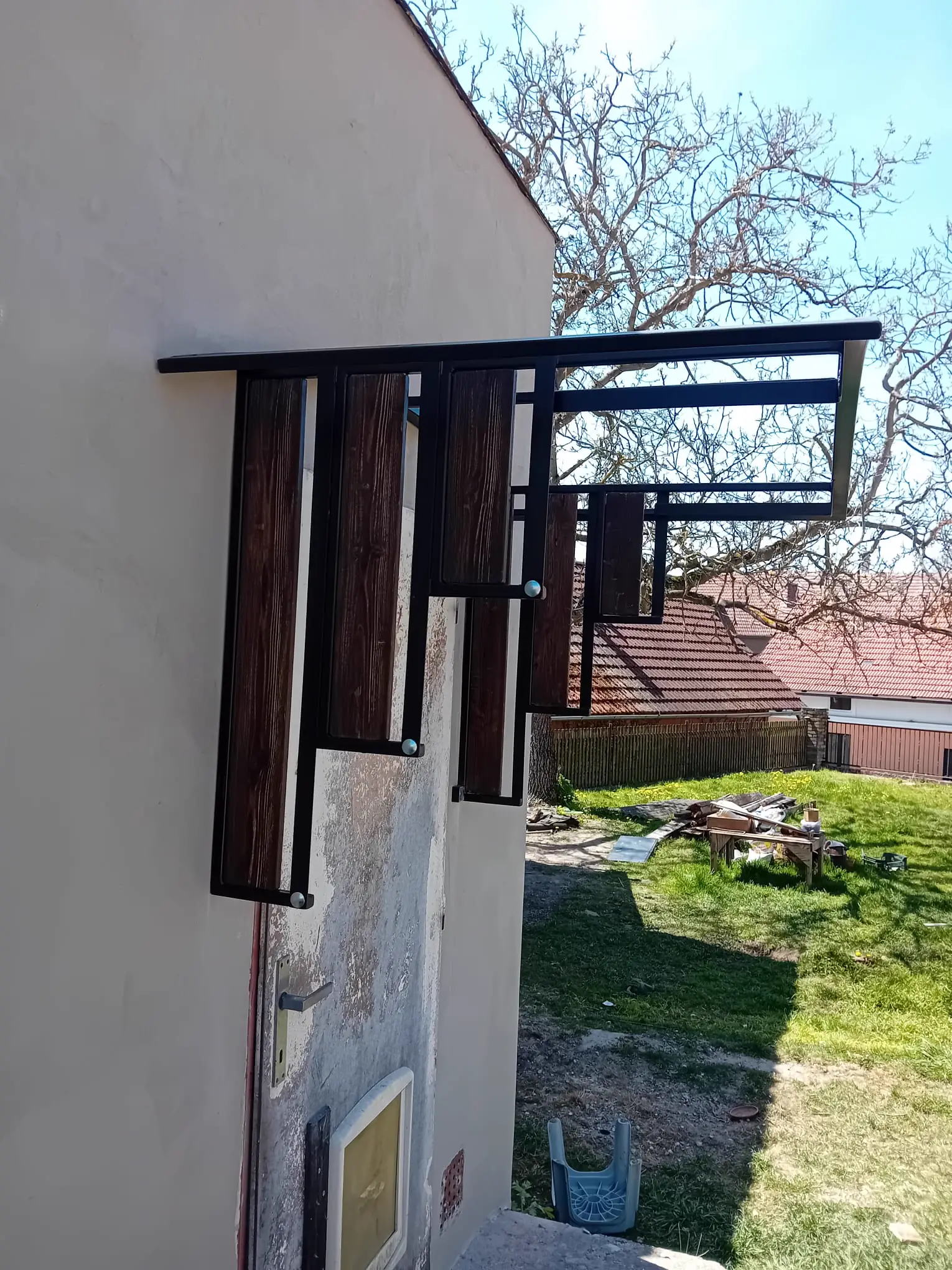 Zastřešení vstupu na stupňovitých ocelových konzolách s výplní z tmavě mořeného dřeva, pohled z boku